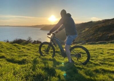 Man on electric mountain bike looking at sunset on coast